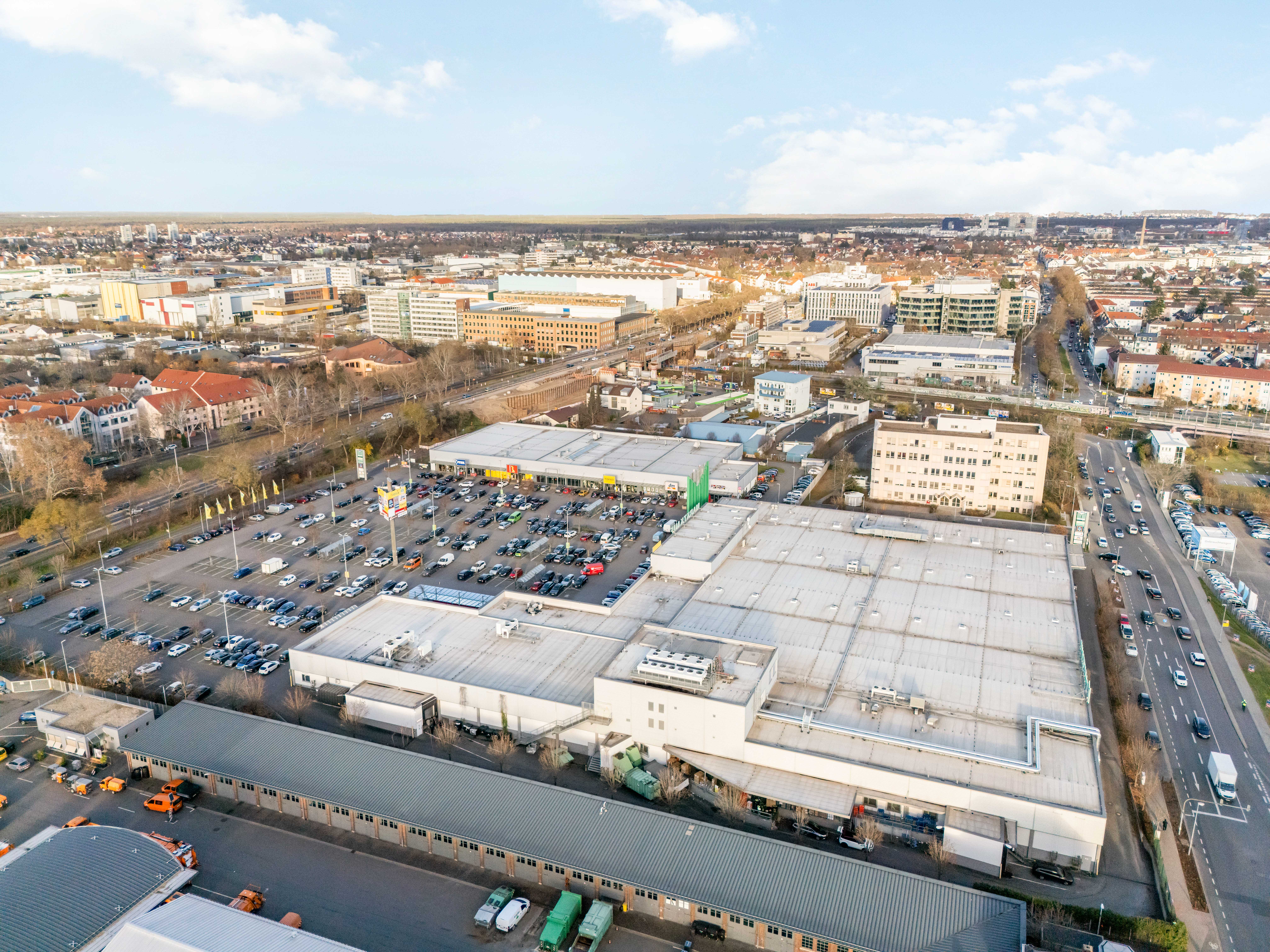 Vor einem REWE-Center-Supermarkt mit roten Eingangsschildern stehen Menschen fahren Autos.