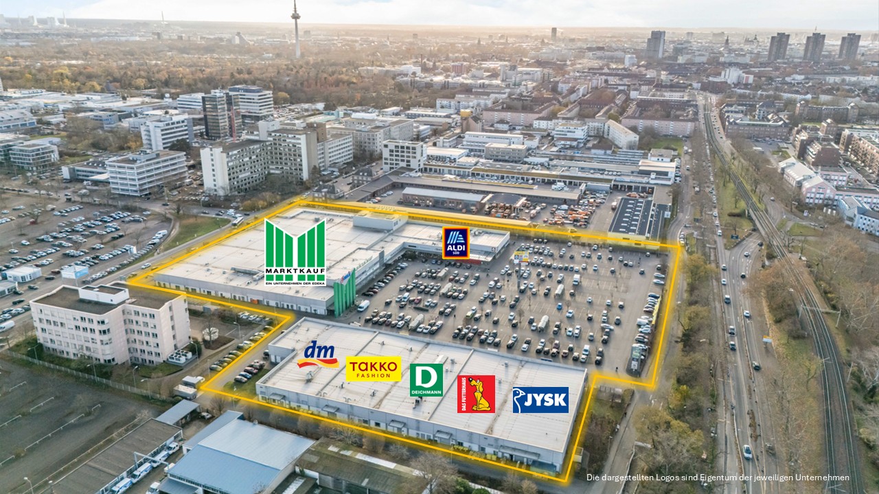 Vor einem REWE-Center-Supermarkt mit roten Eingangsschildern stehen Menschen fahren Autos.