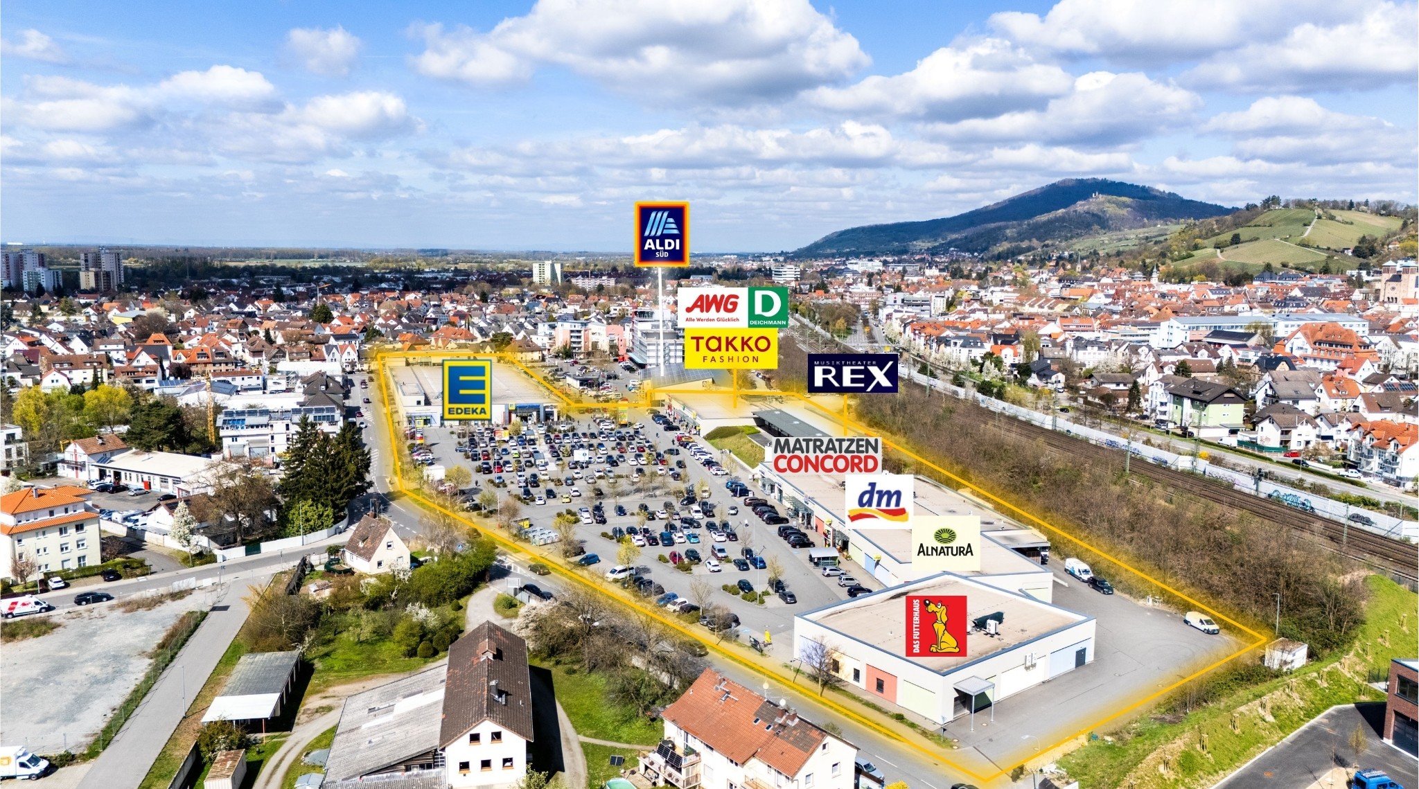 Vor einem REWE-Center-Supermarkt mit roten Eingangsschildern stehen Menschen fahren Autos.